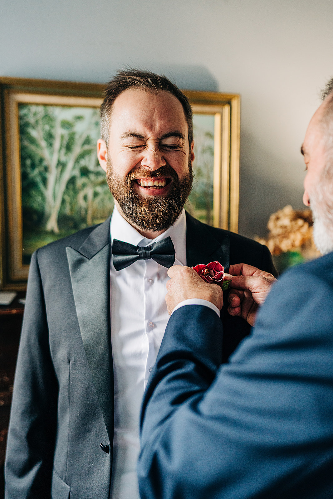groom laughing while brides dad attaches flower to jacket