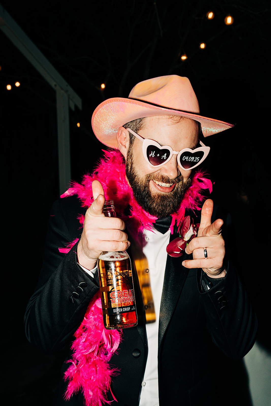 groom in pink cowboy hat and pink boa giving finger guns