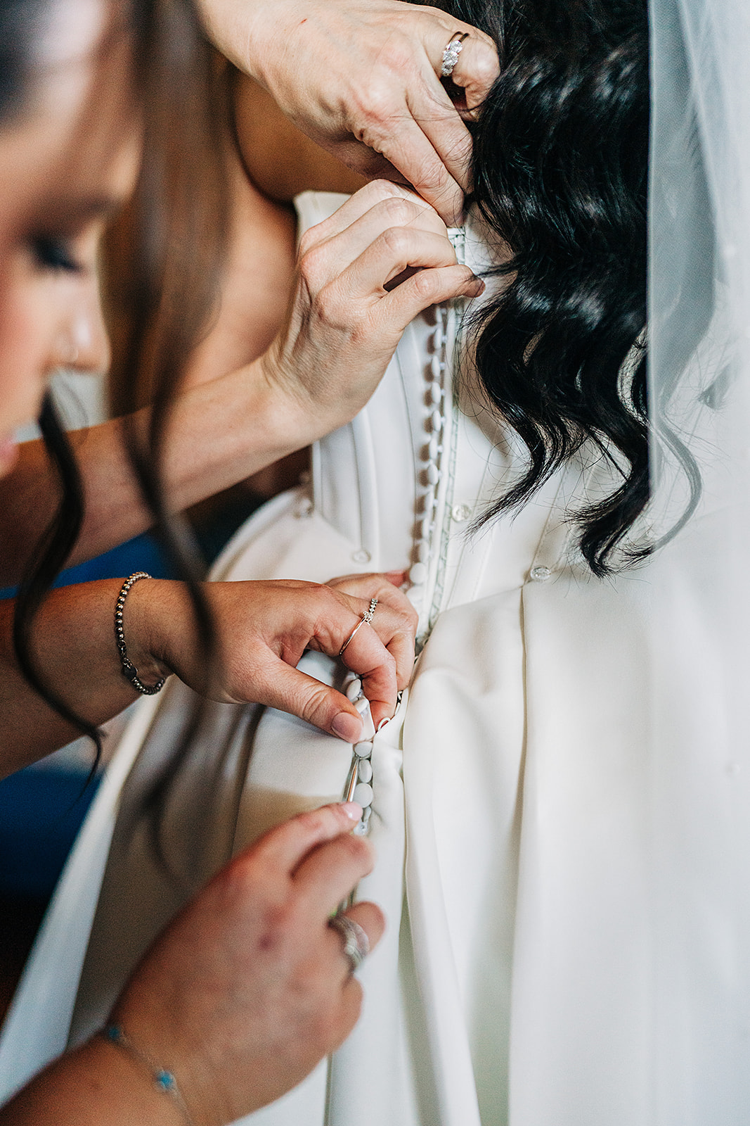 two sets of hands doing up the buttons on brides dress